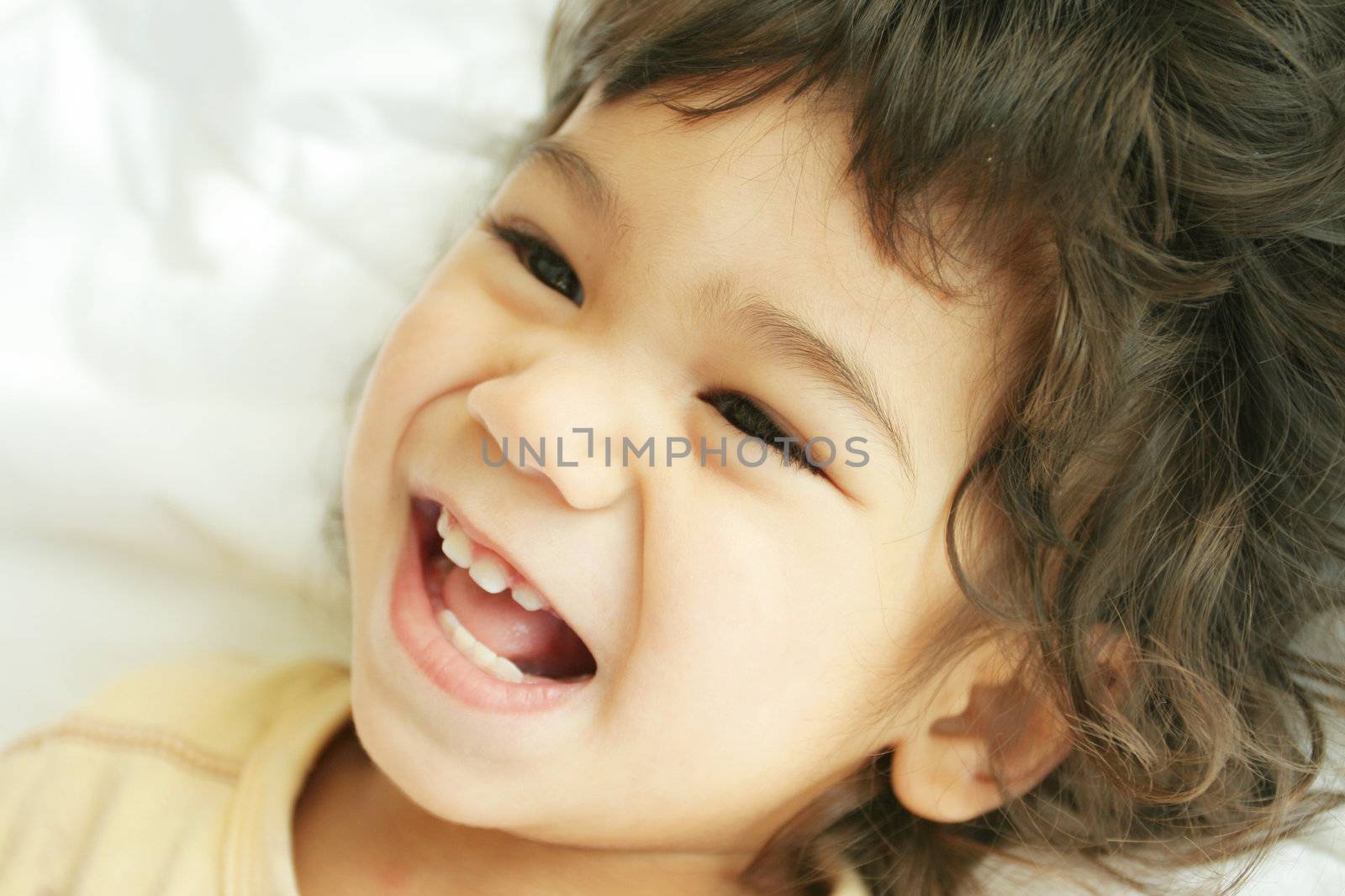 Beautiful toddler boy lying on bed laughing and smiling. Part asian, scandinavian descent.