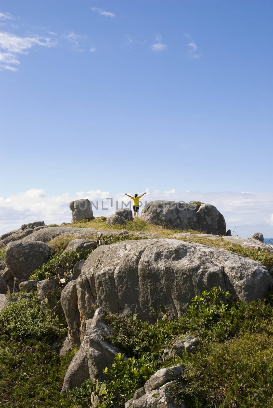 Adult woman photographed from behind with arms open on top of a rocky hill.