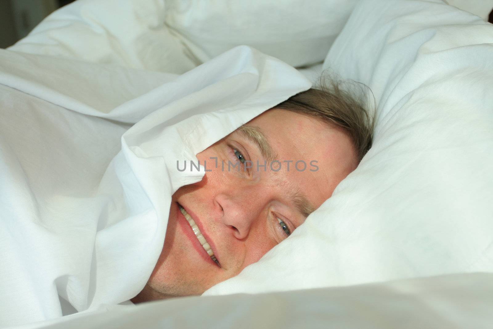 Man sleeping under white covers,  waking up in the morning light