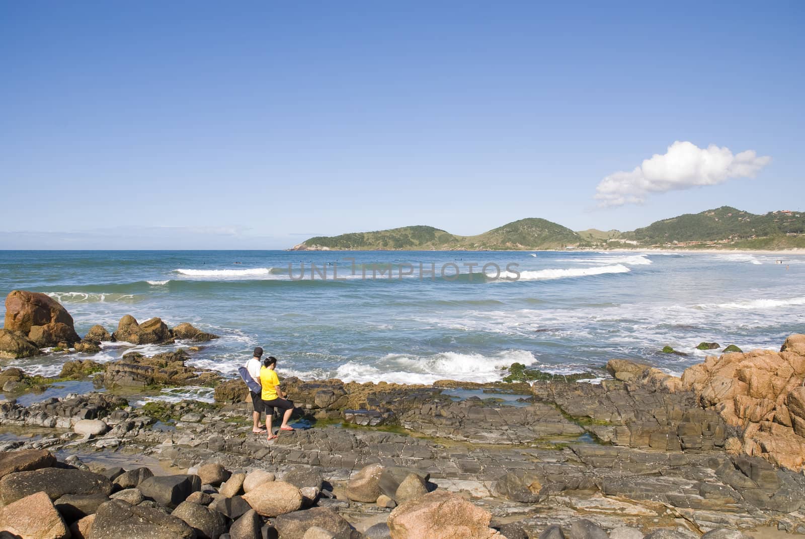 Adult couple in the coastline looking out into the sea, with clear blue sky.