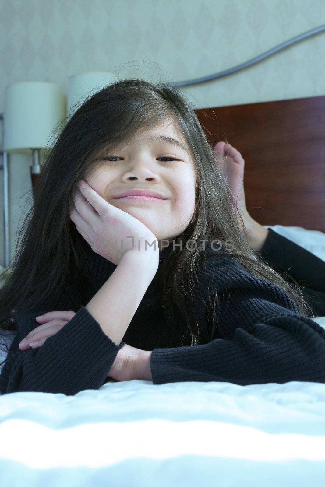 Six year old girl chin on hands thinking while lying down on bed