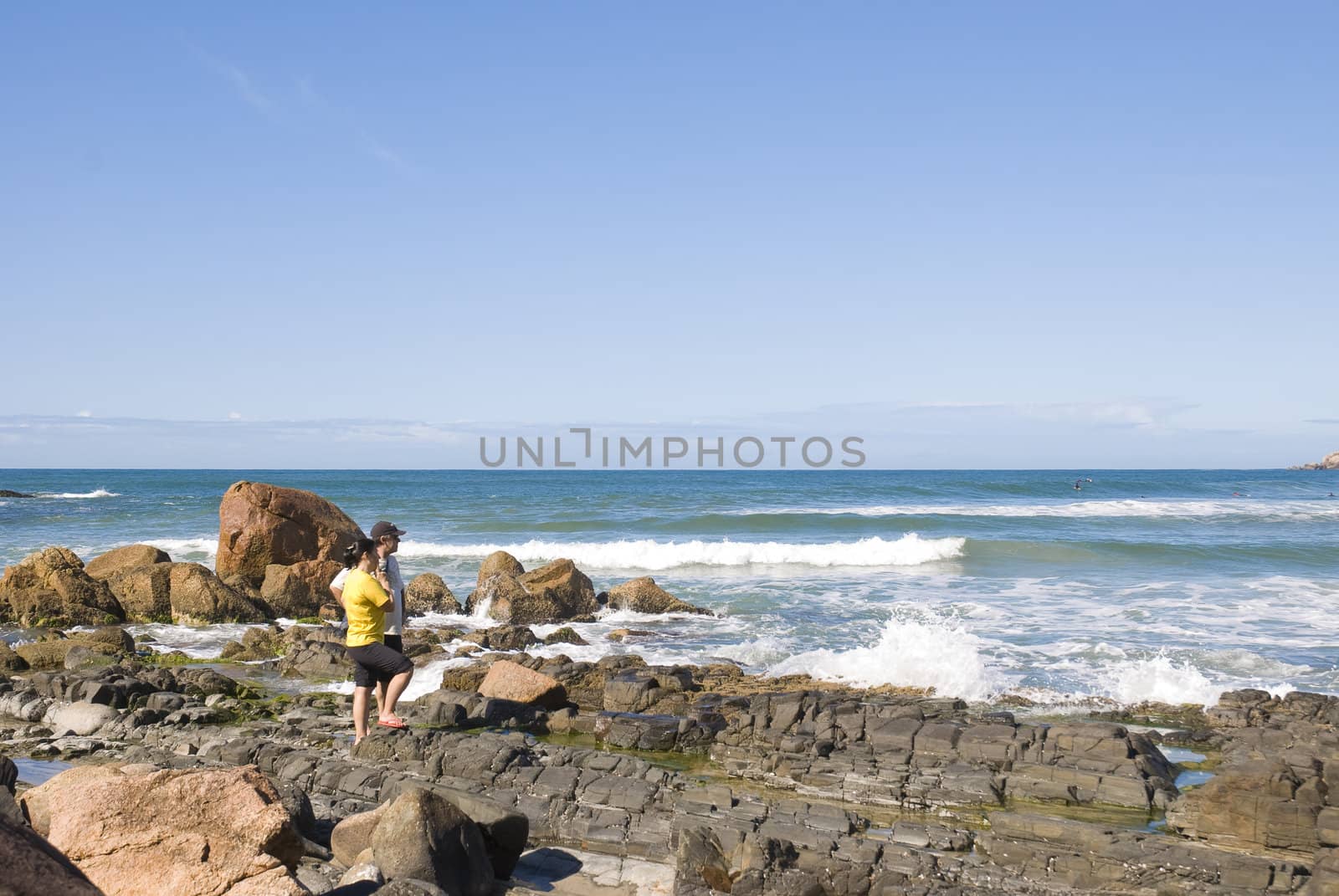 Adult couple in the coastline looking out into the sea, with clear blue sky.