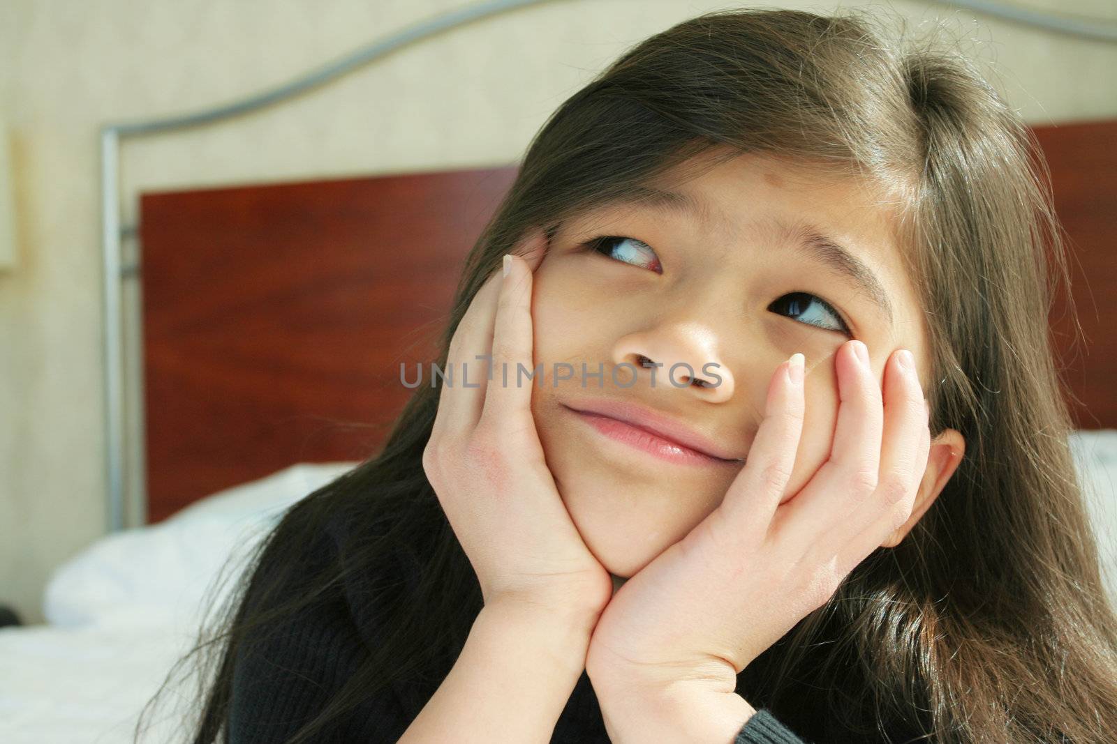 Six year old girl chin on hands thinking while lying down on bed