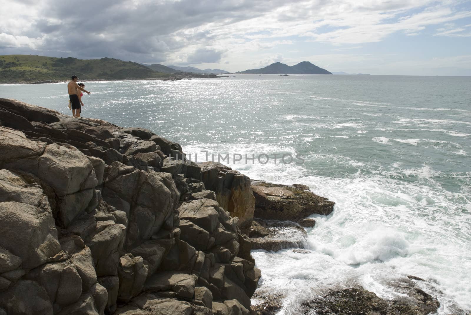 Adult couple standing on a rocky cliff with raging sea beneath.