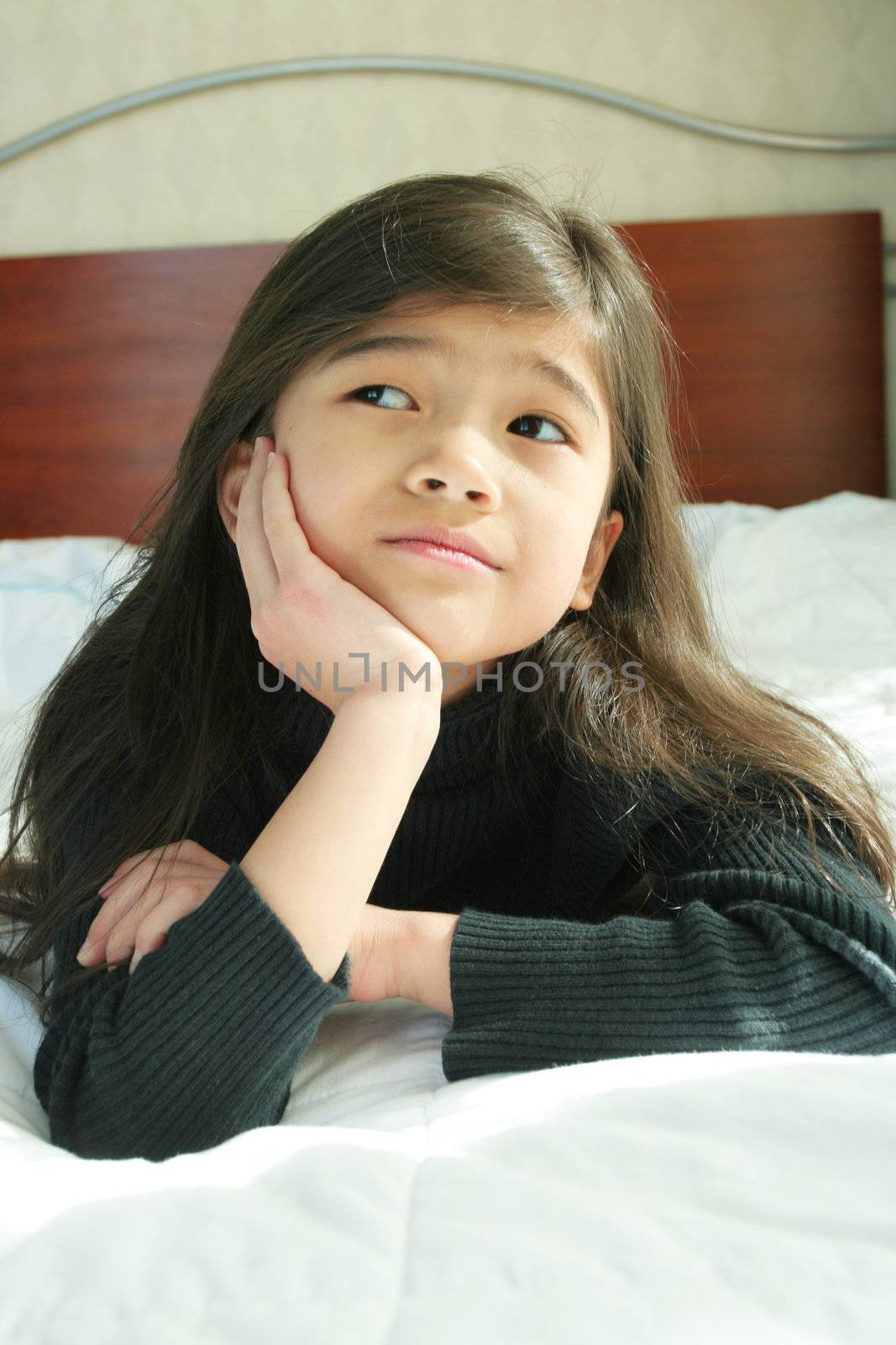 Six year old girl chin on hands thinking while lying down on bed