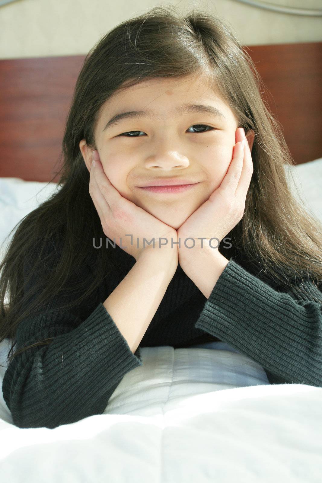 Six year old girl chin on hands thinking while lying down on bed