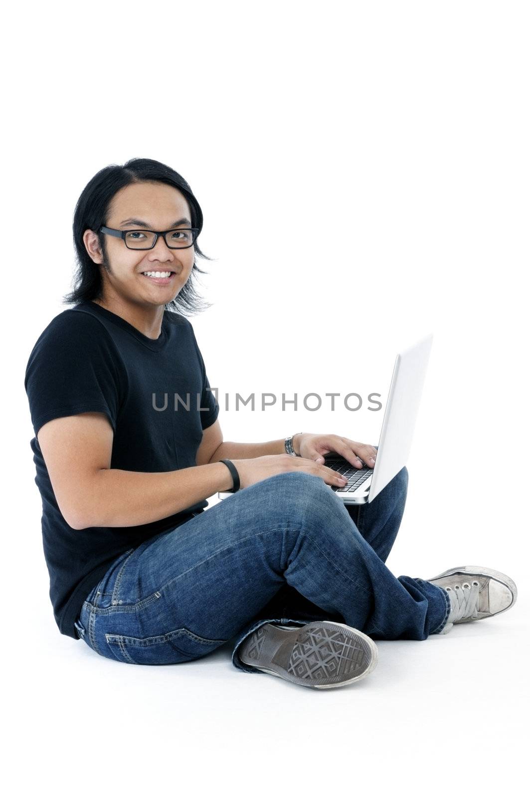 Handsome young Asian man sitting on floor with laptop over white background.