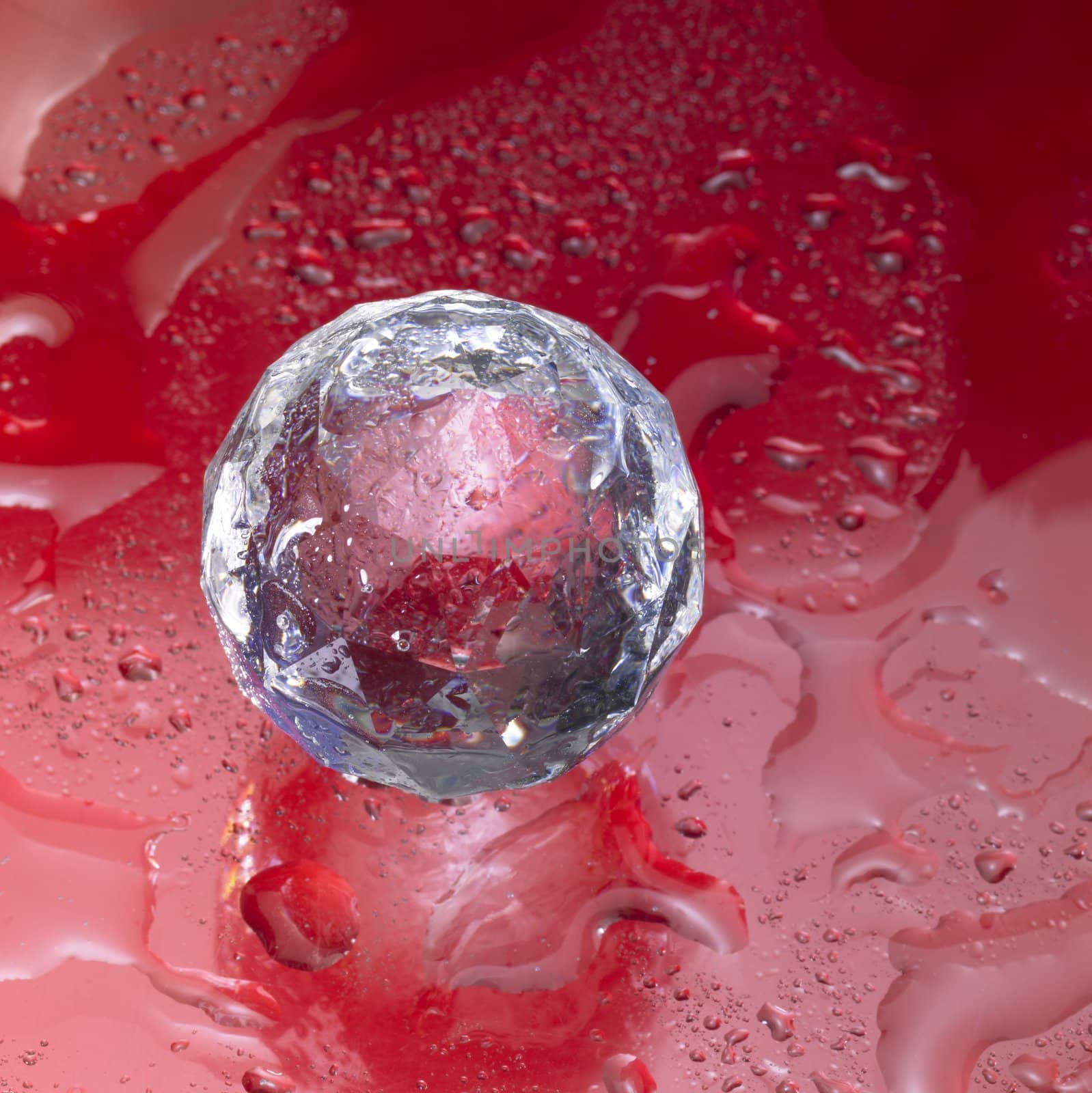 Studio photograpgy of a diamond ball made of glass in red back with water drops