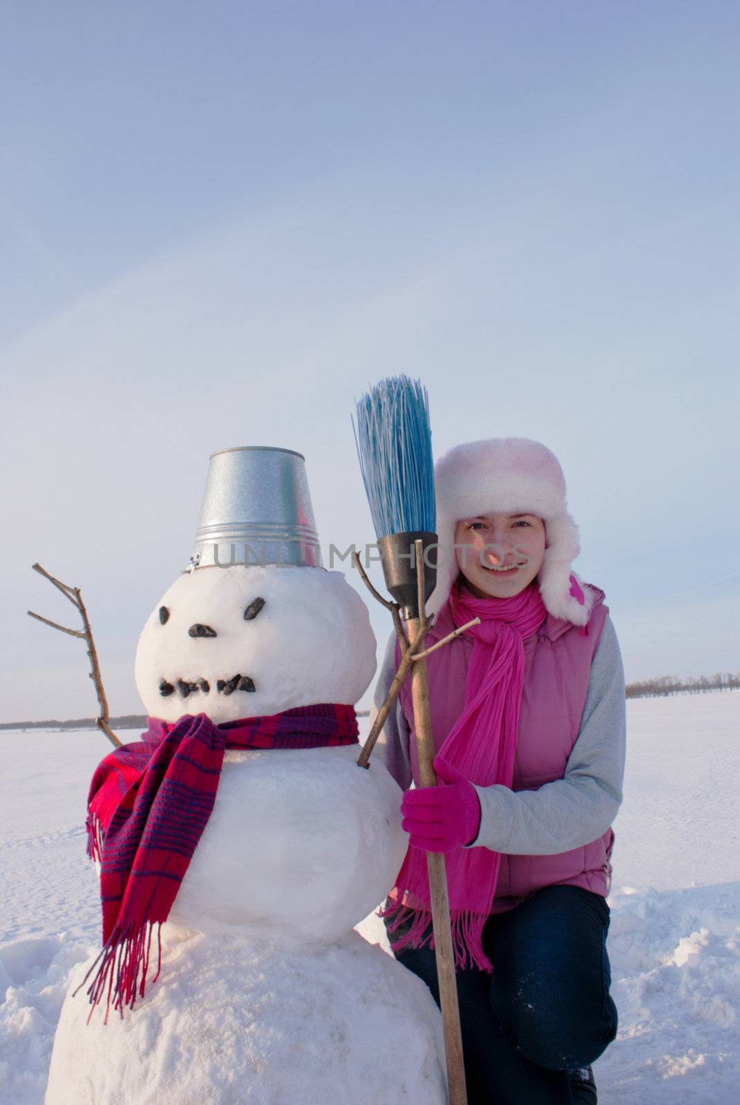 Teenage girl with snowman at winter time