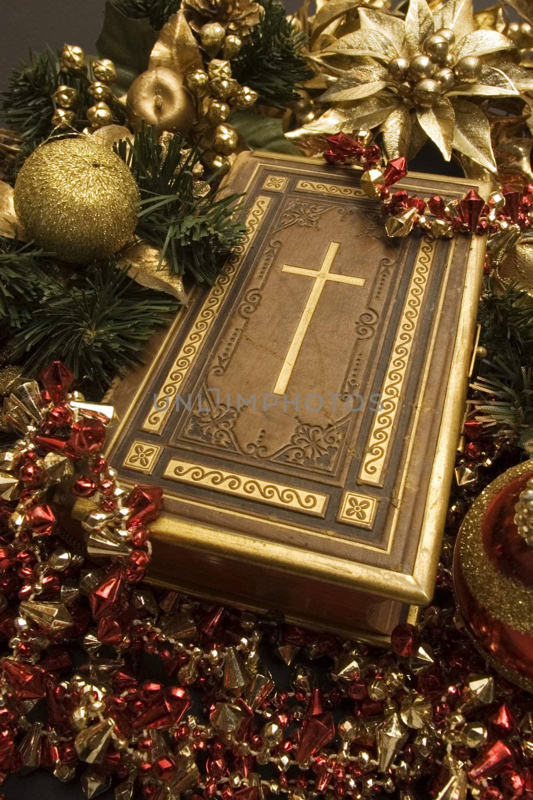 Bible with selective focus on the cross placed around Christmas ornaments.
