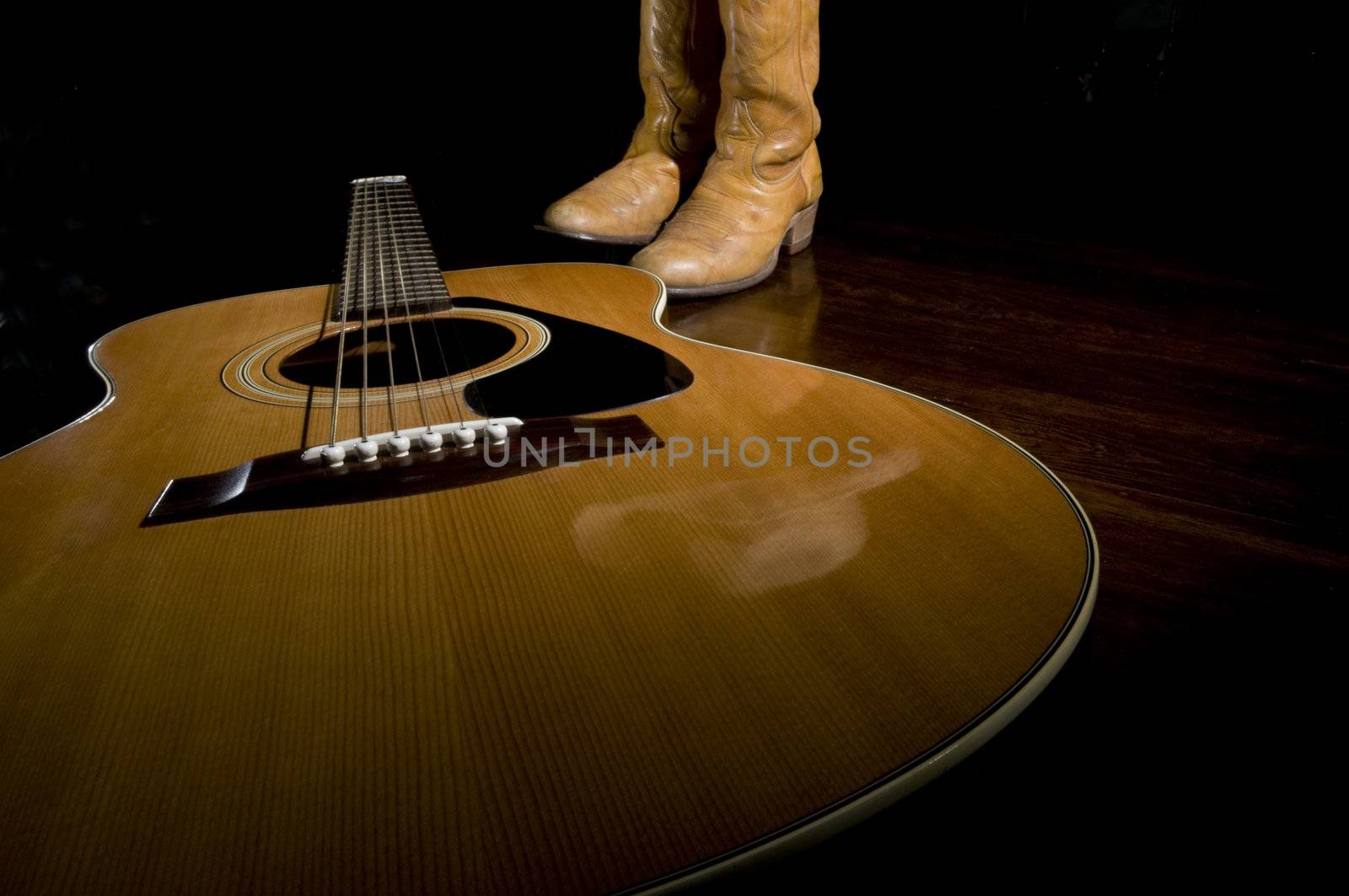 Selective focus on the guitar in the foreground with cowboy boots in the background
