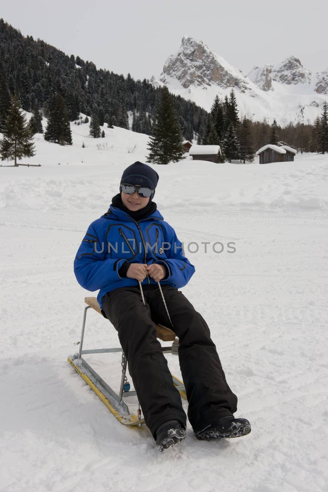 Young boy on a sledge on a snowy trail in val di fassa, in the dolomites