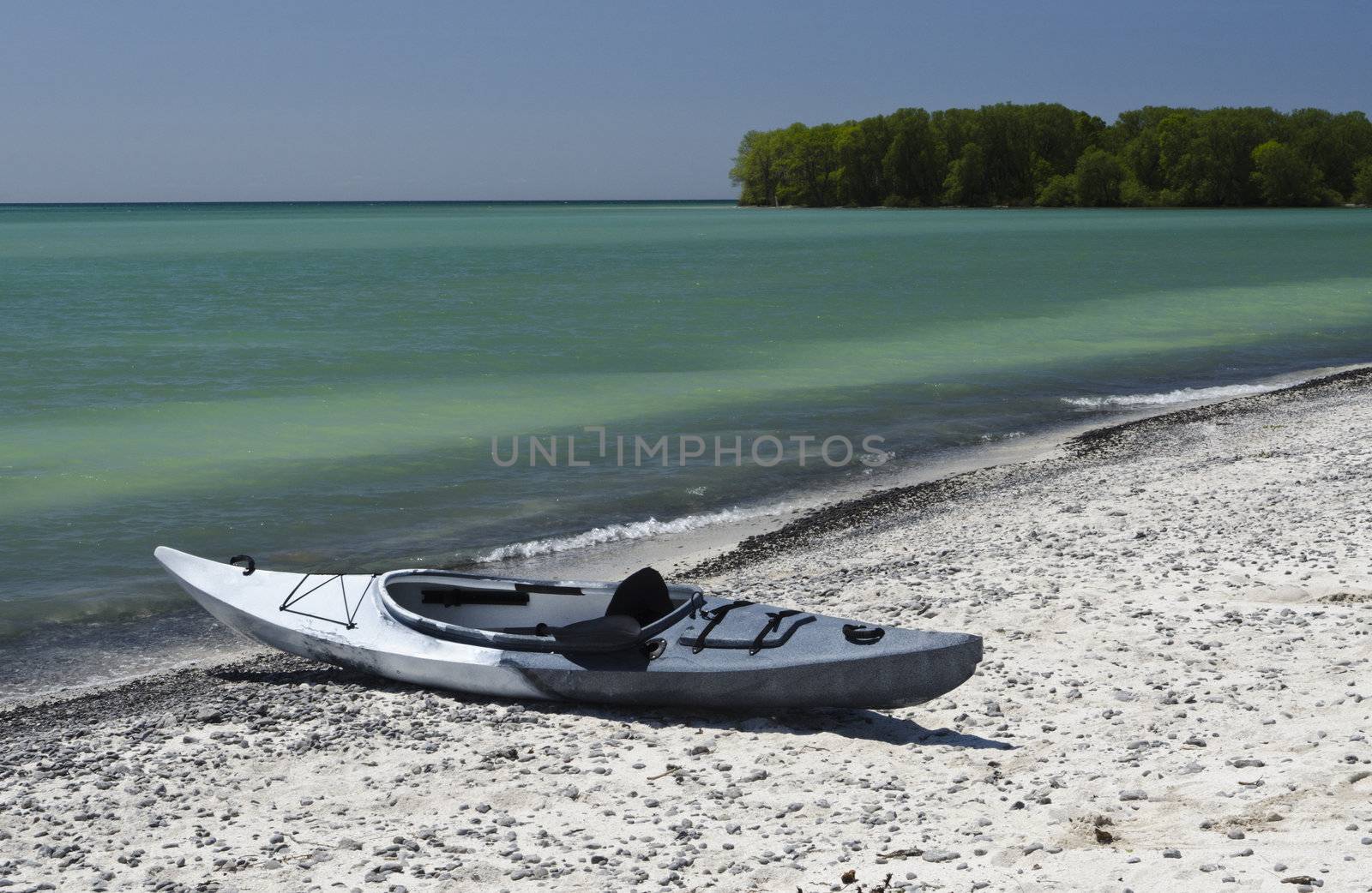 Kayak sitting on the sandy shoreline with deep blue sky and emerald coloured Lake Ontario 