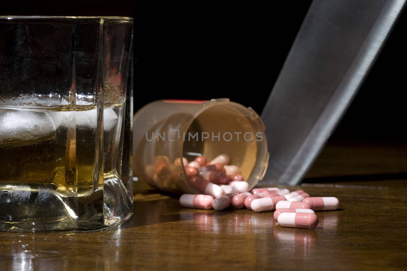 Alcohol and pills in the foreground with a knife sticking out the table in the background