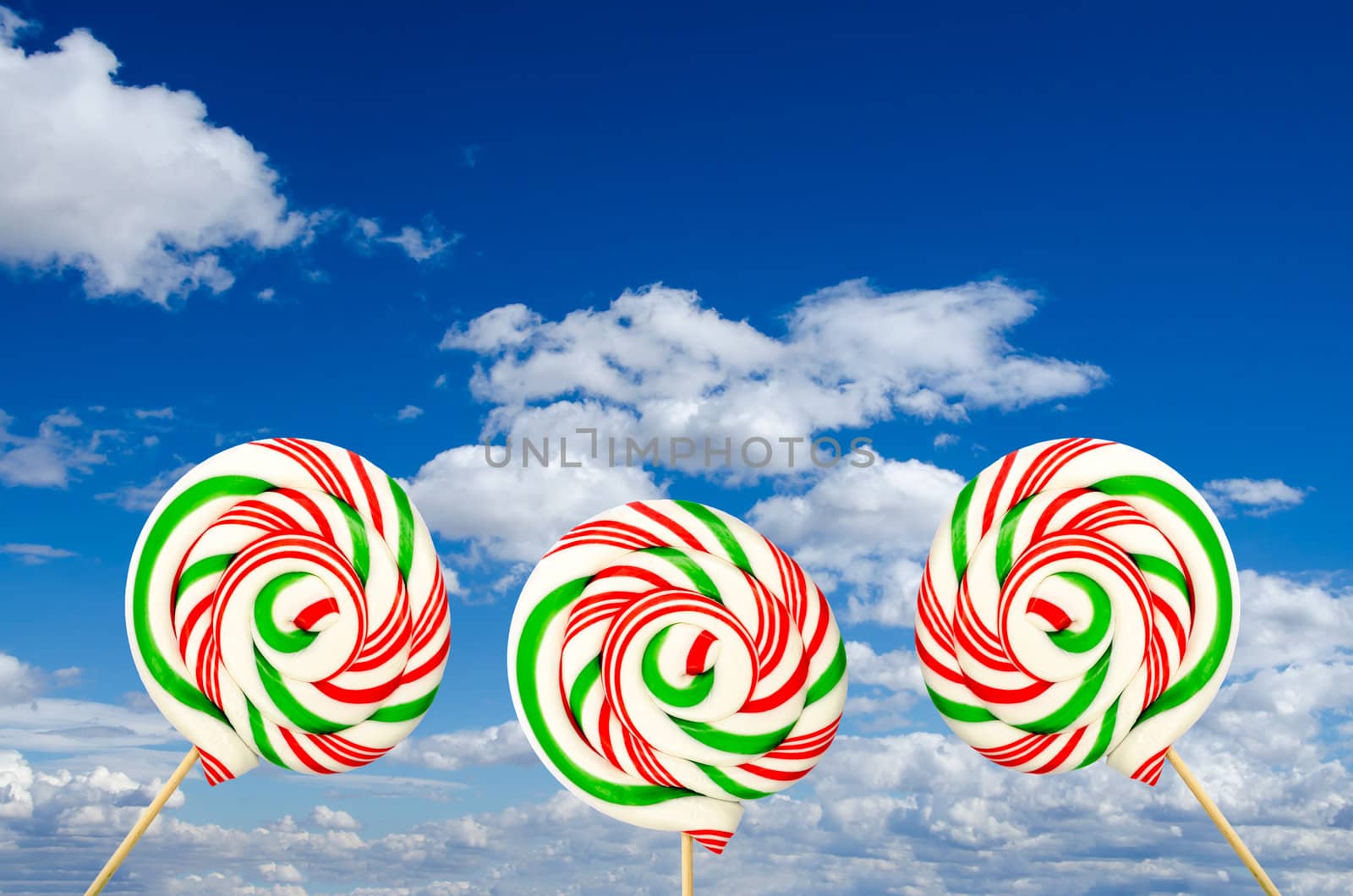 Three sugar lollipops in white green and red on background of sky and clouds