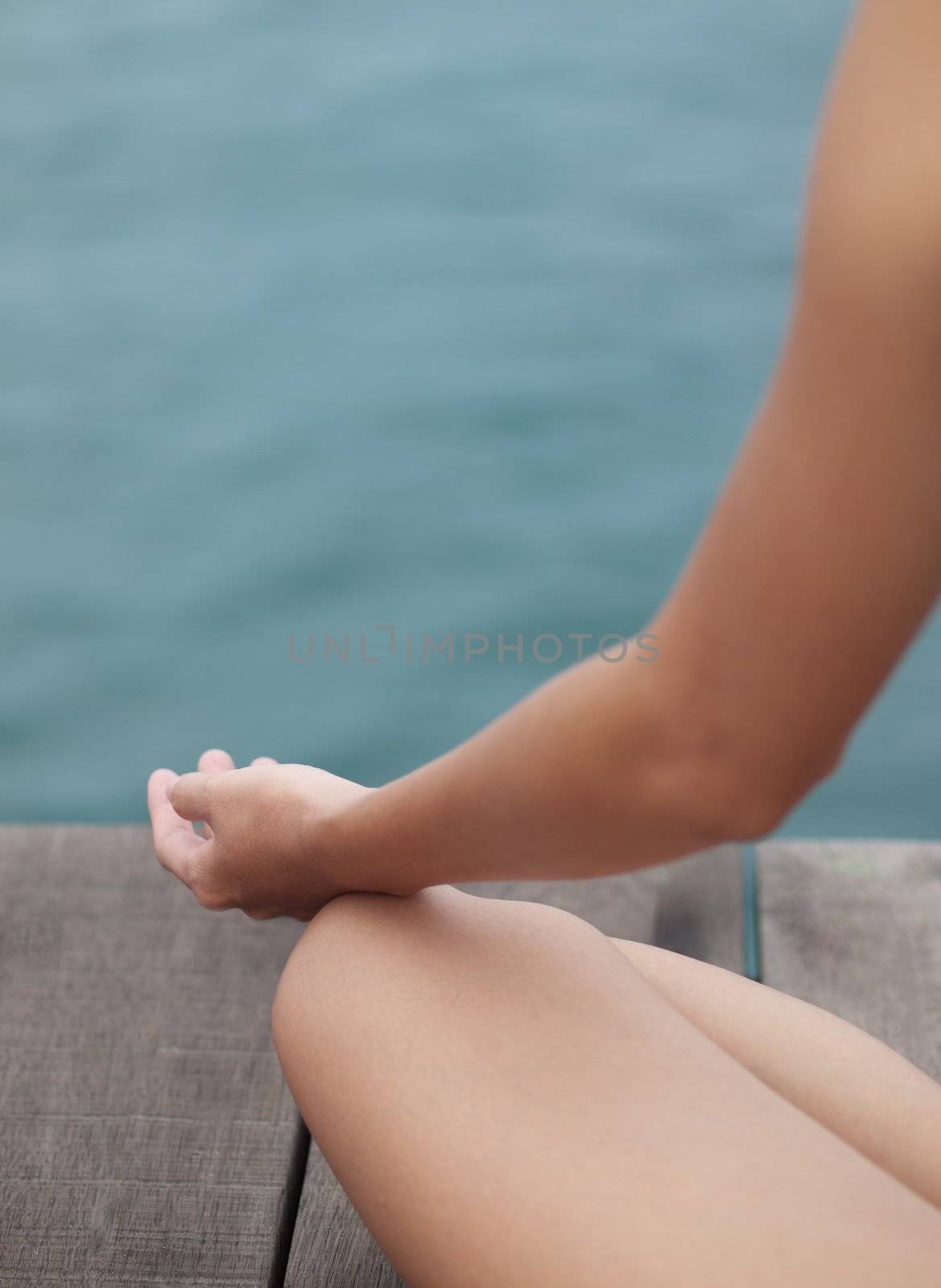 Young woman meditating on the lotus position on a pier beside the ocean