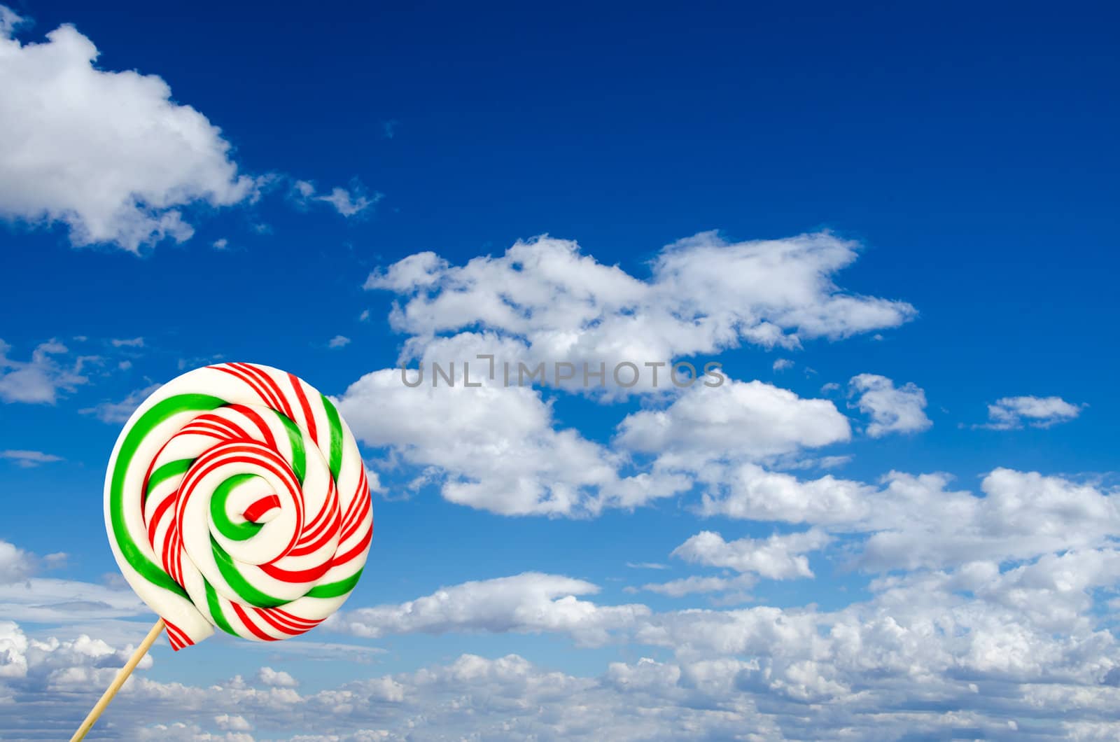 Single sugar lollipop in white green and red on background of sky and clouds