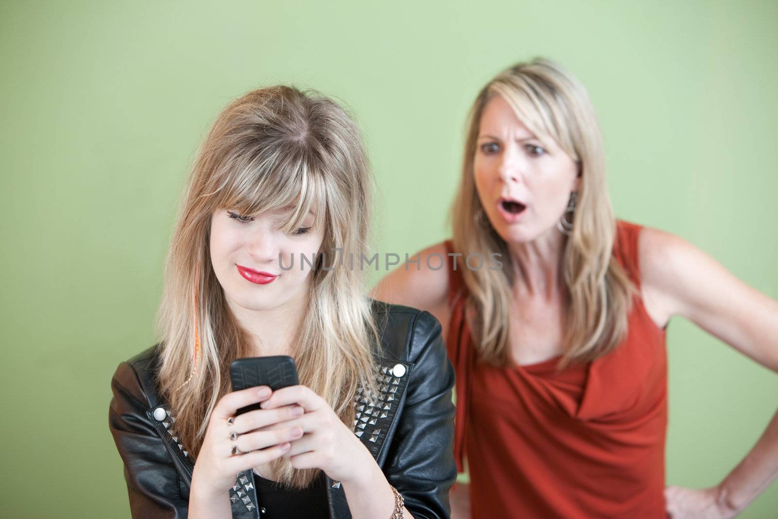 Shocked mom watches teen use phone over green background