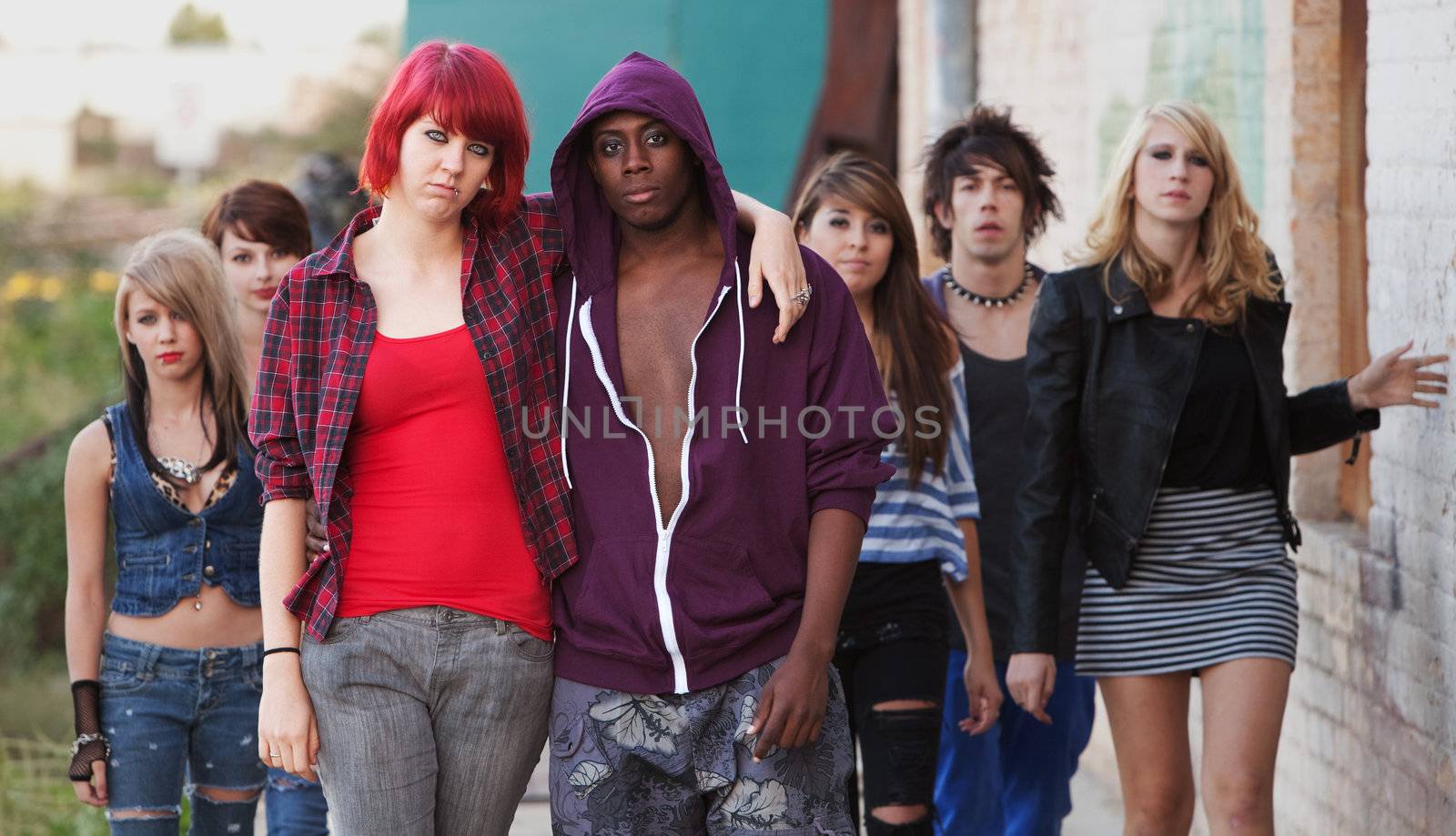A pair of young punk teens pose together as their friends stay in the background.