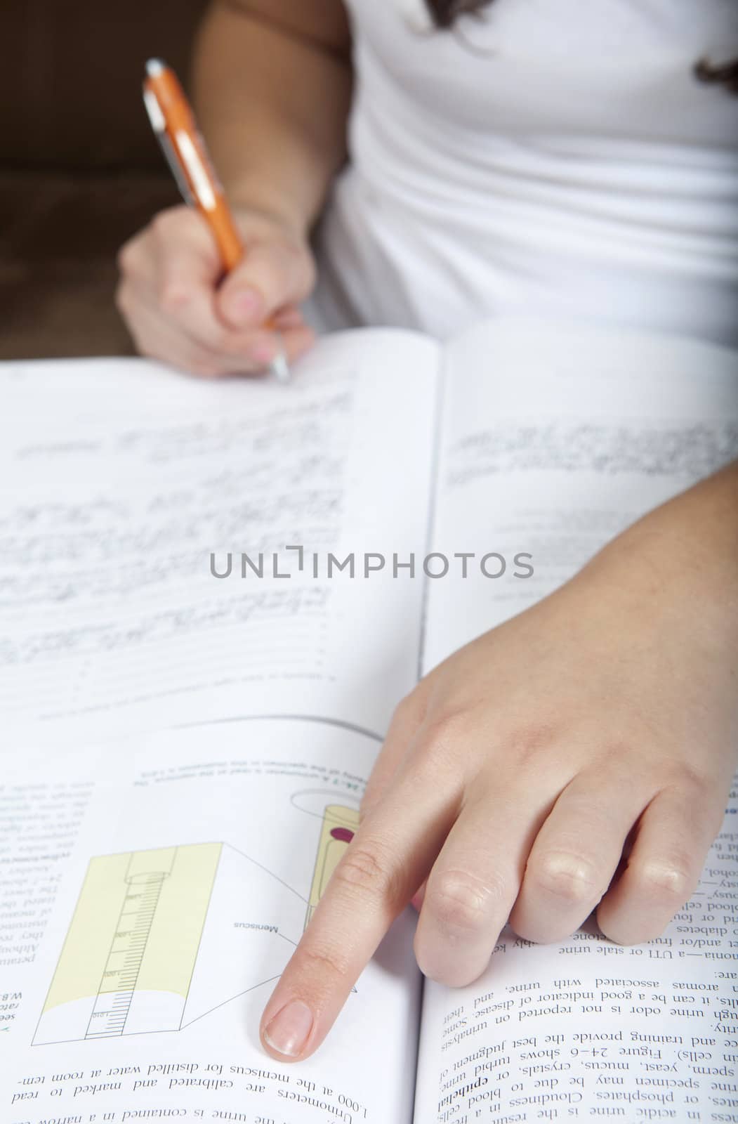 Close up of a young woman doing homework in a textbook, while writing and taking notes at the same time.