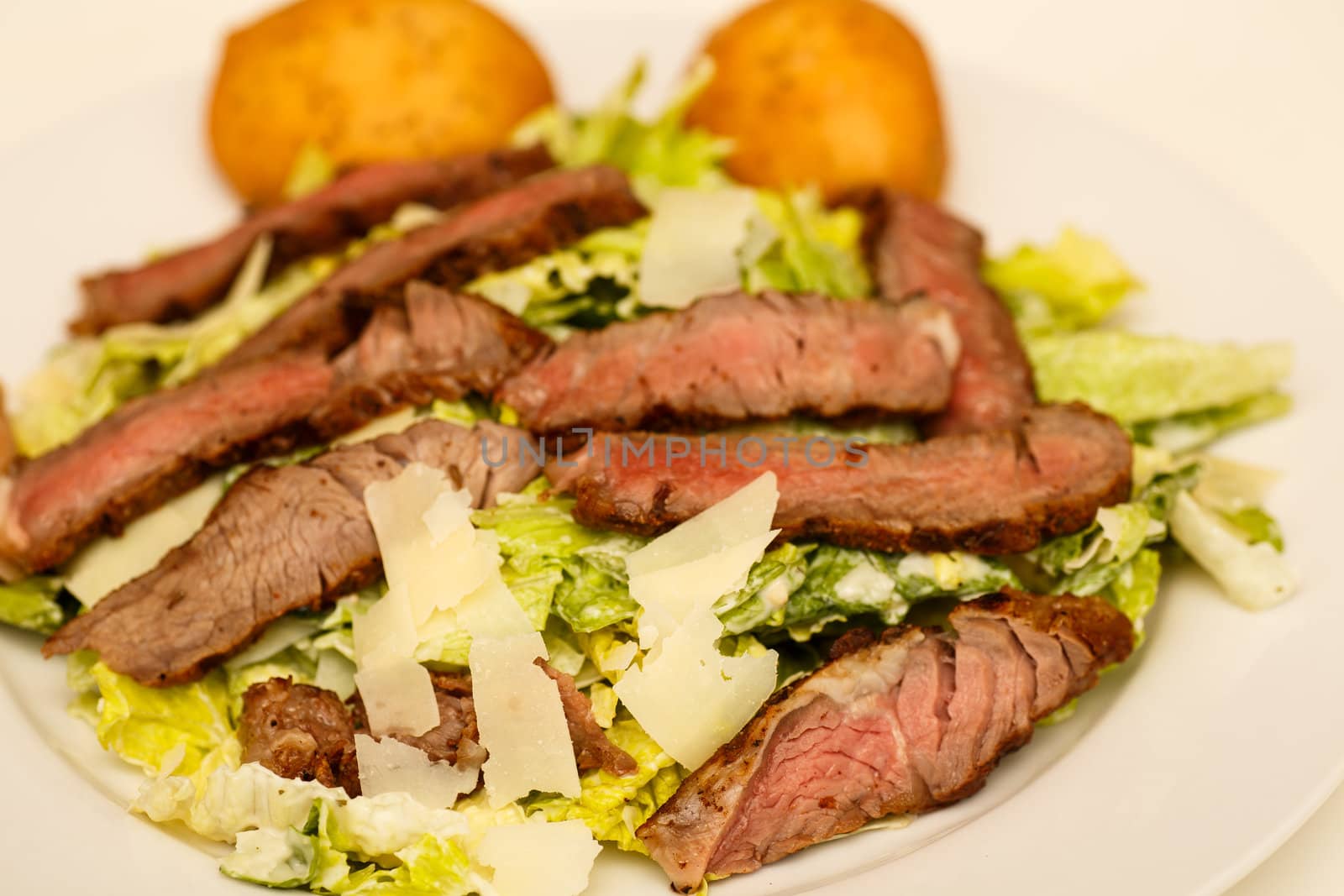 A fresh caesar salad with strips of medium-rare beef and two muffins