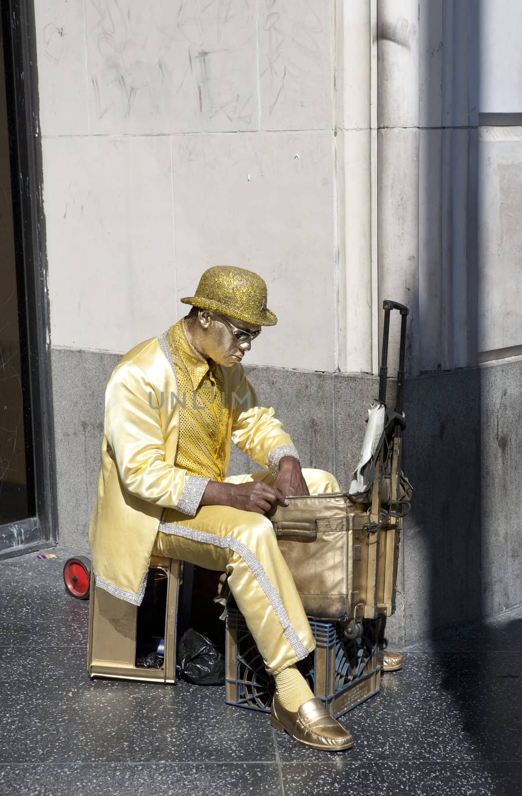 Street performer covered in gold paint getting ready to perform on a sidewalk on Hollywood Blvd.