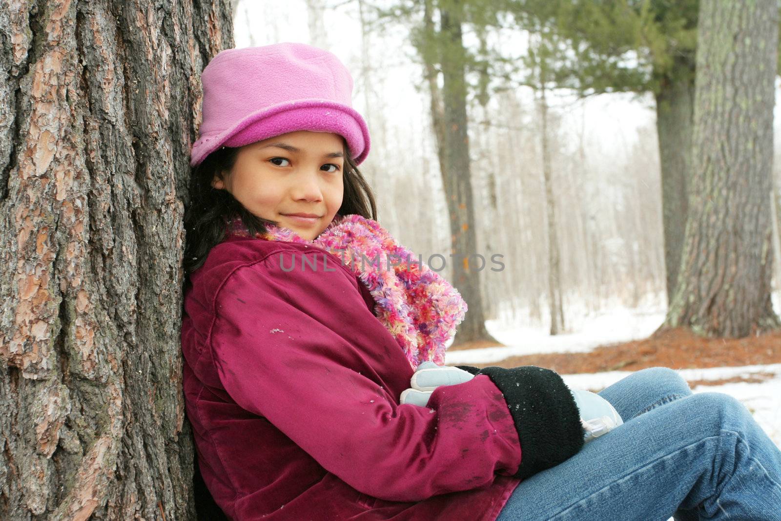 Nine year old girl sitting against tree in winter