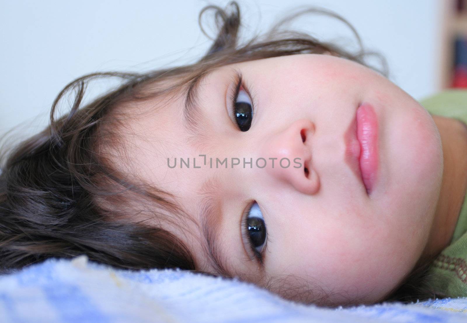 Sweet quiet toddler boy lying down looking gently around. Part Scandinavian, Thai background