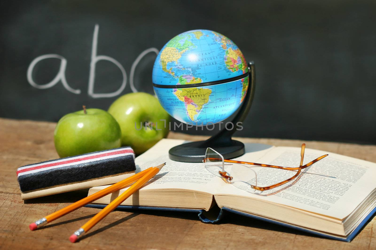 School books and apple in front of school chalkboard with small atlas