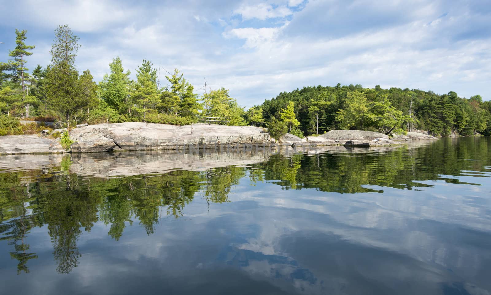 Reflection on a calm lake of a rocky shoreline of a northern lake