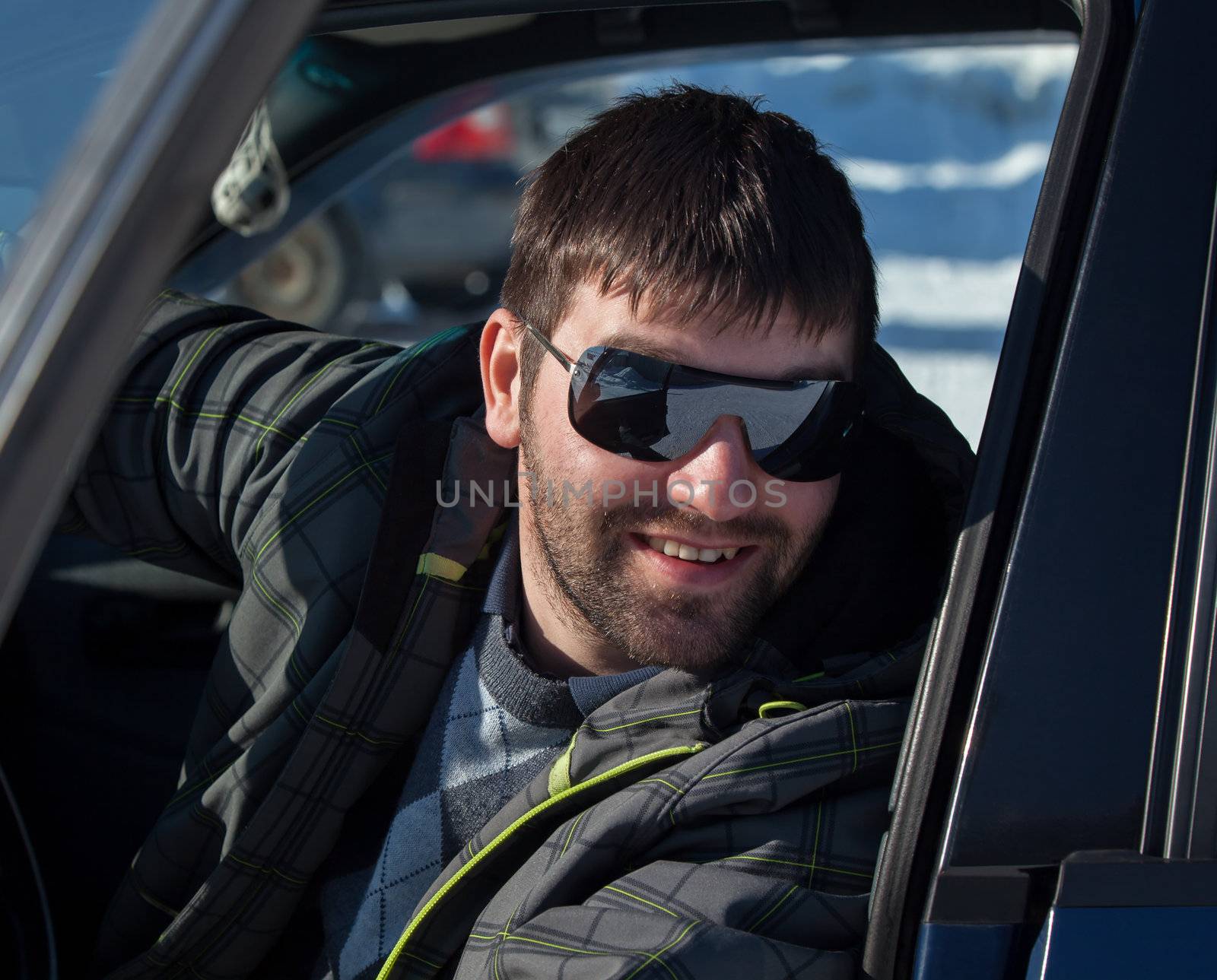 A young man wearing sunglasses in a private car. Bright sun, spring, good mood