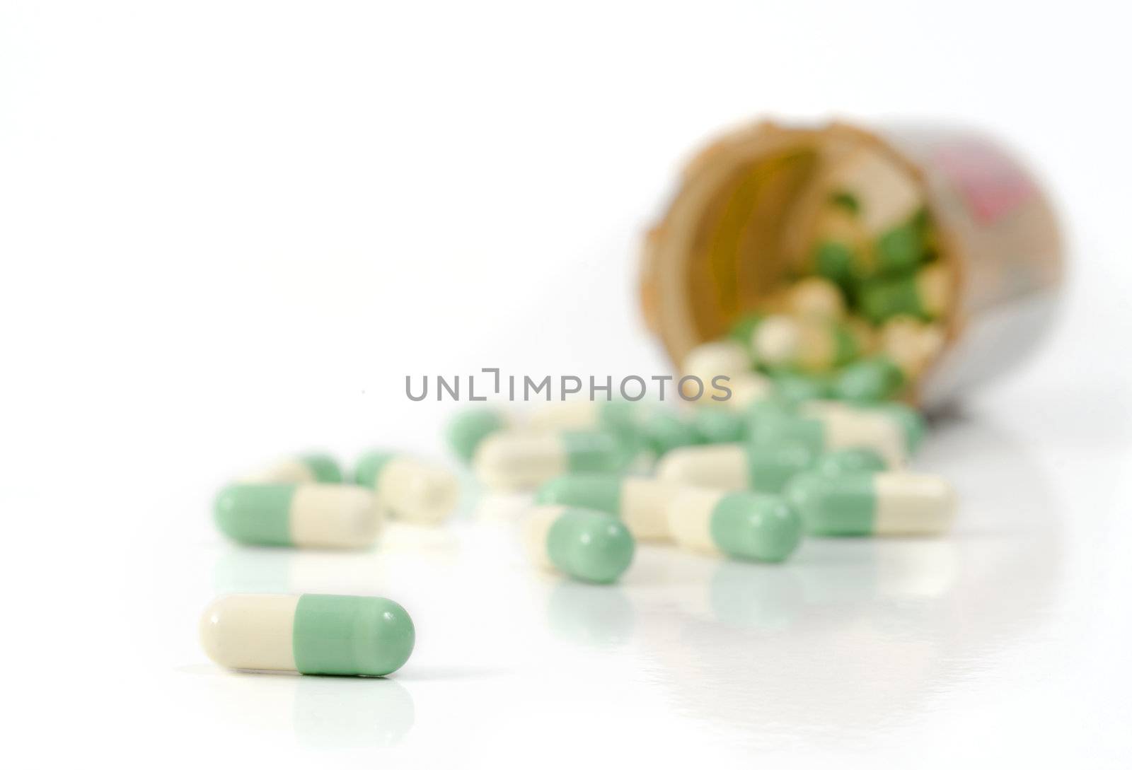 Selective focus on the foreground capsules spilled out of the pill bottle onto the white background