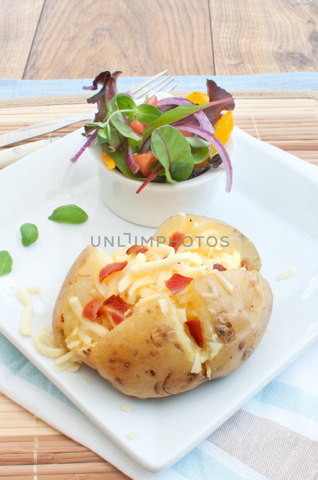 Melting cheese and bacon pieces with baked potato and salad in a bowl