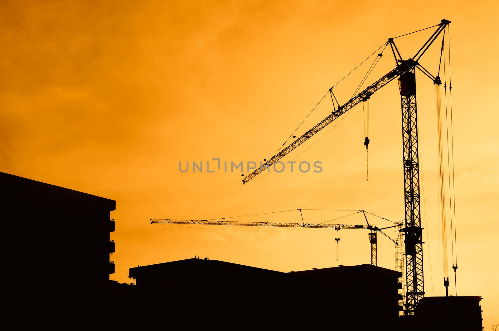 Construction site silhouetted against orange sunset, sky added in photoshop