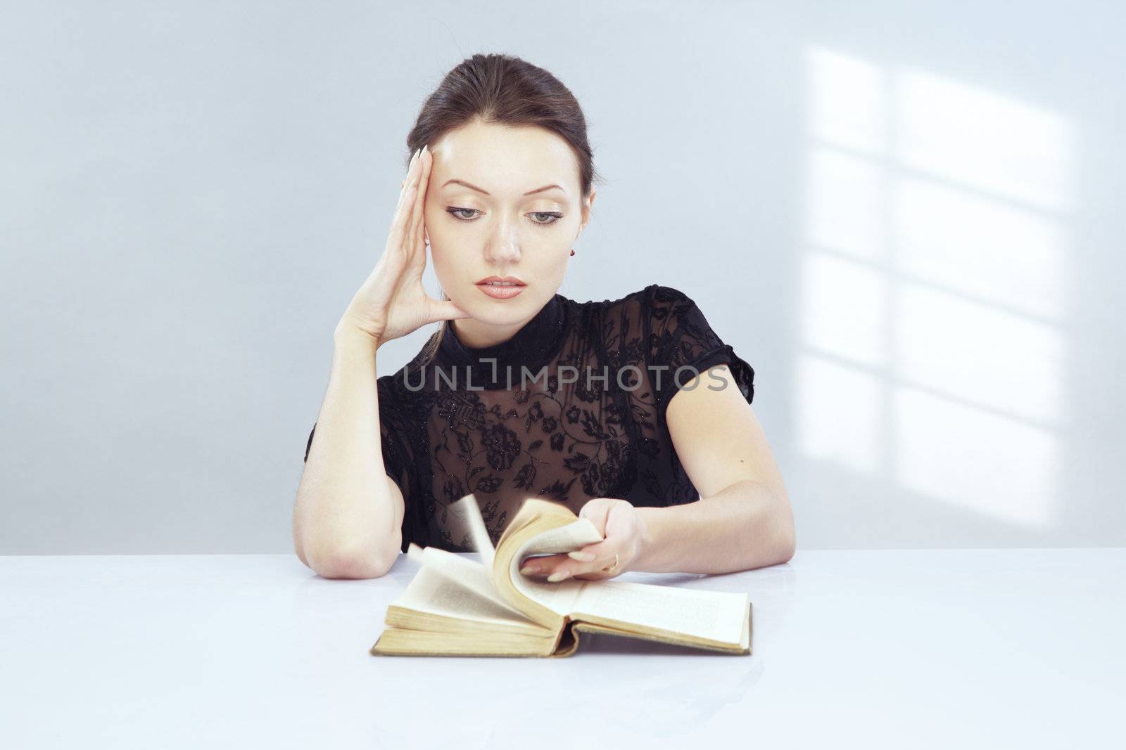Young clever woman indoors reading textbook. Shadow from window on the wall