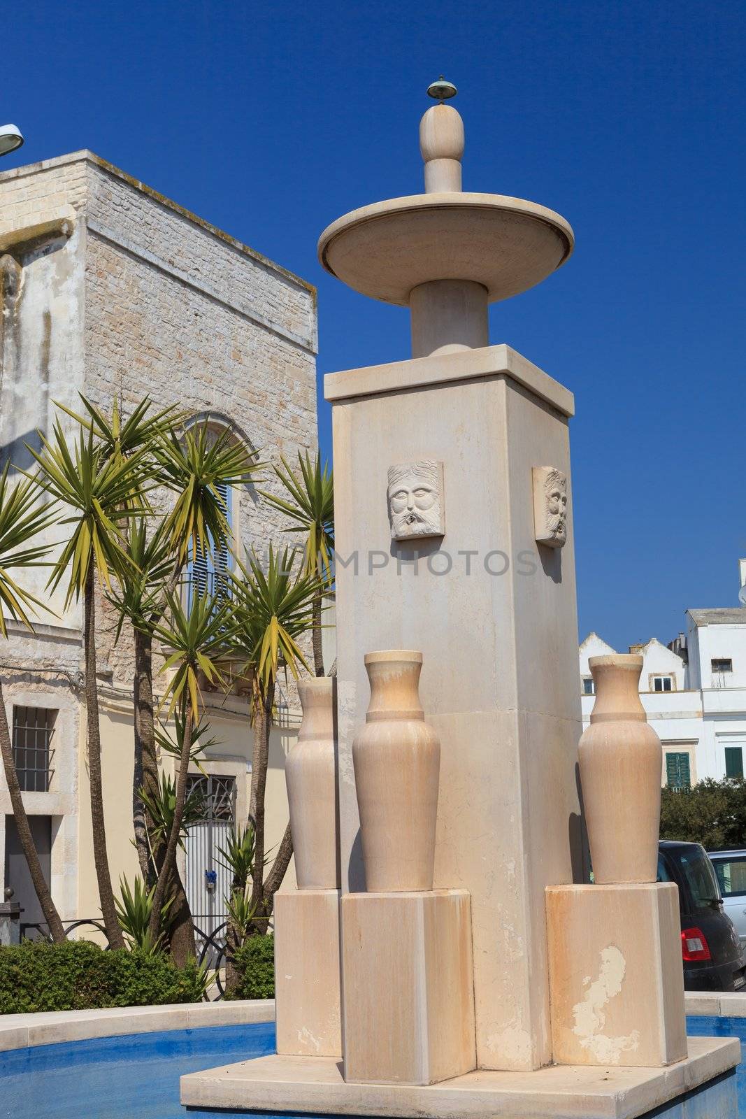 Two carved stone faces on a tall water fountain in Alberobello