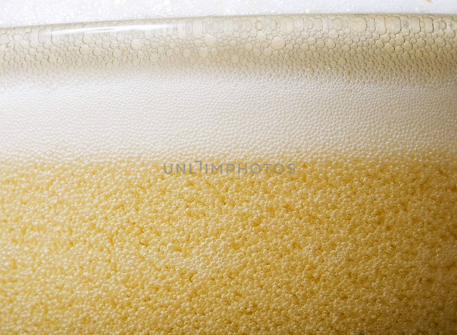 Macro shot of the top of a glass of beer with lots of foam and bubbles.