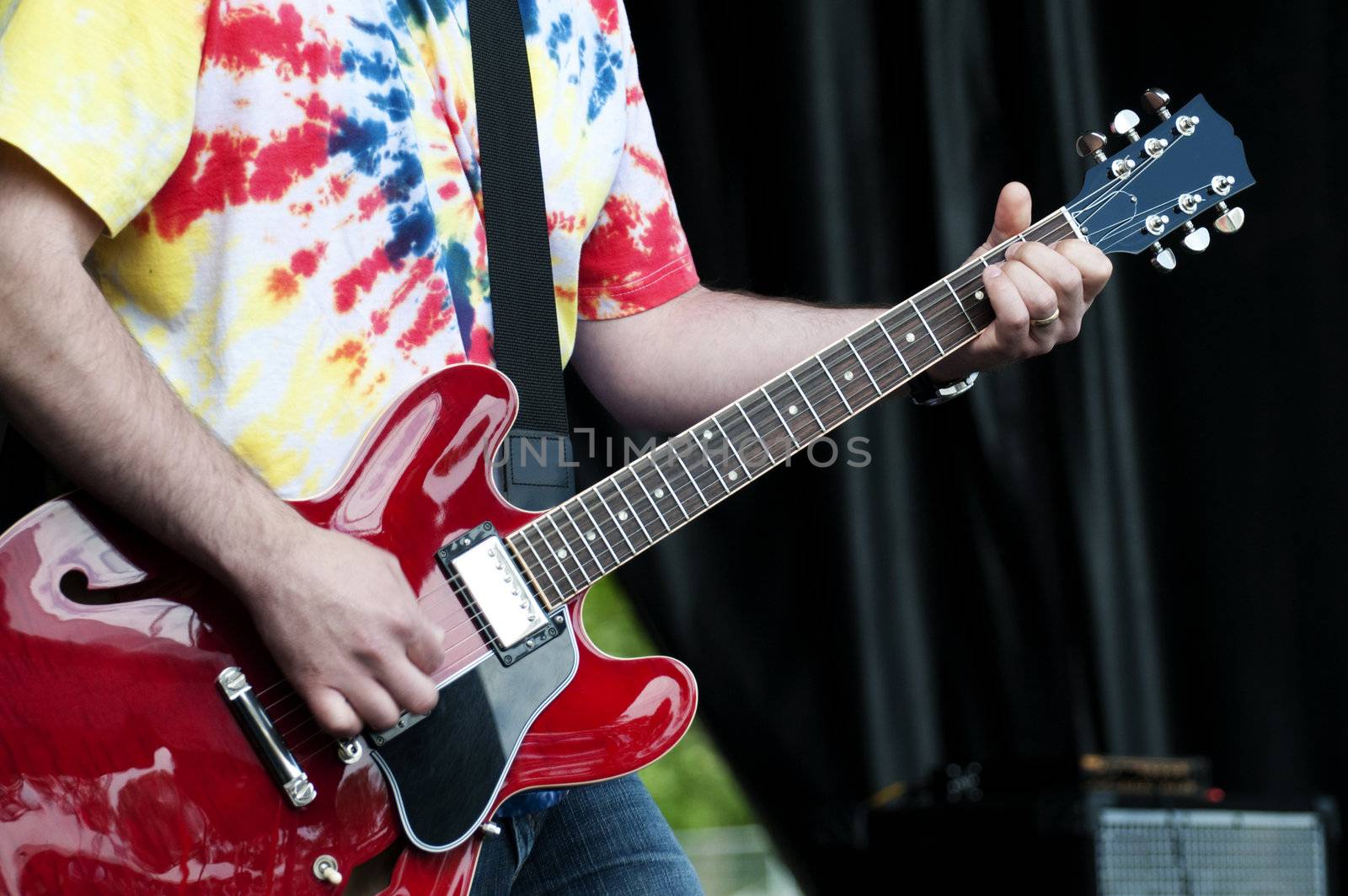 Young musician playing an acoustic/electric guitar at a music festival, highlighting 60's style clothes