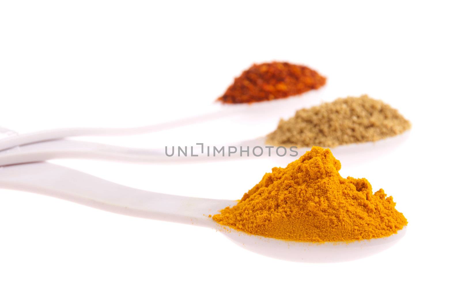 indian spices in measuring spoons (curcuma, coriander, red pepper flakes) isolated on white background (shallow DOF, focus on first)