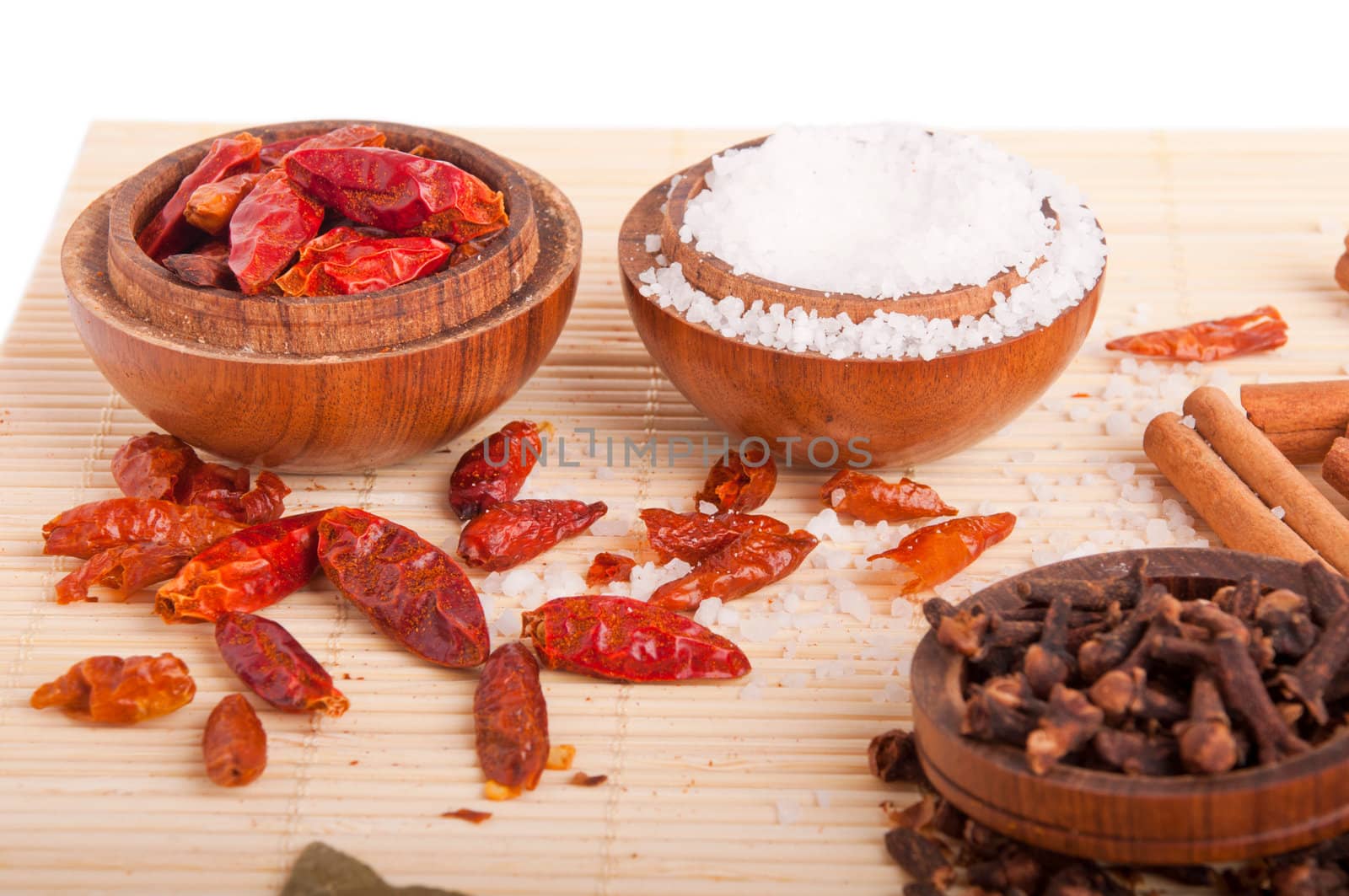 gorgeous setting with cooking spices and herbs (cloves, cinnamon sticks, piri piri, salt) on wooden bowls and mat (isolated on white)