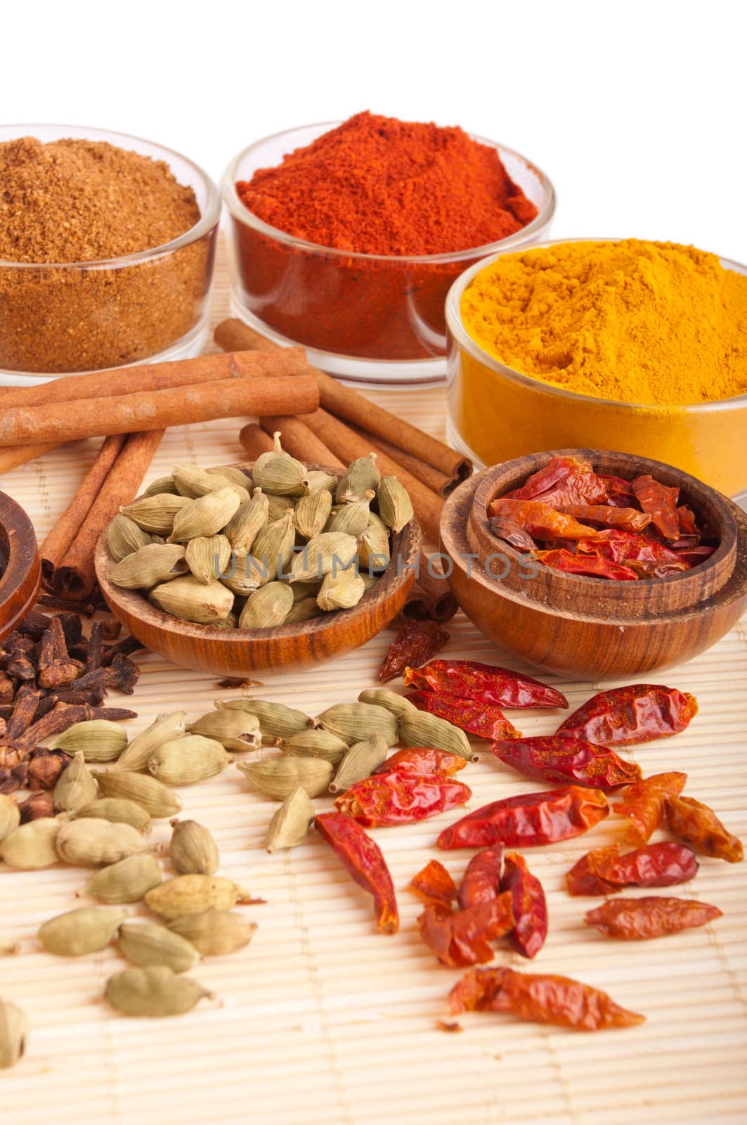 gorgeous setting with cooking spices and herbs (cloves, cardamom pods, cinnamon sticks, garam masala, paprika, piri piri, turmeric) on a wooden mat (isolated on white background)