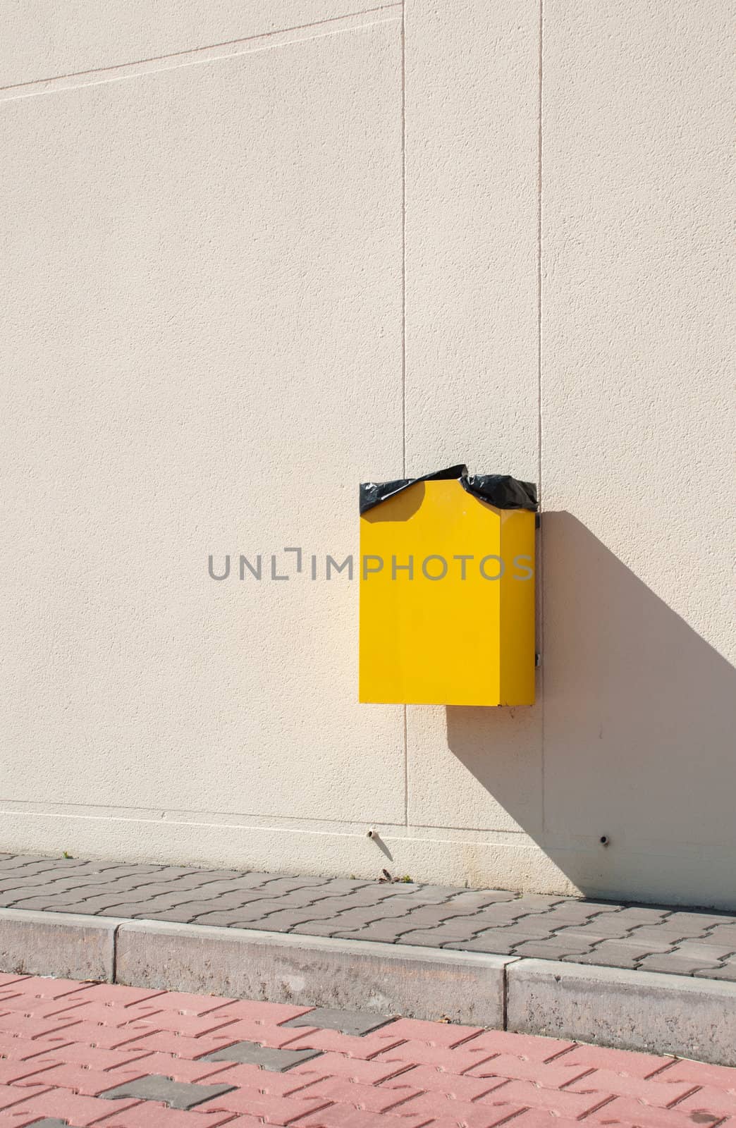 yellow garbage can hanging on wall at a urban sidewalk