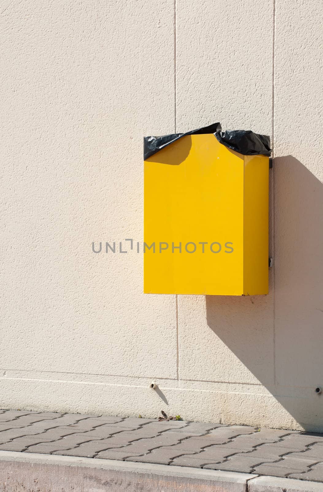 yellow garbage can hanging on wall at a urban sidewalk