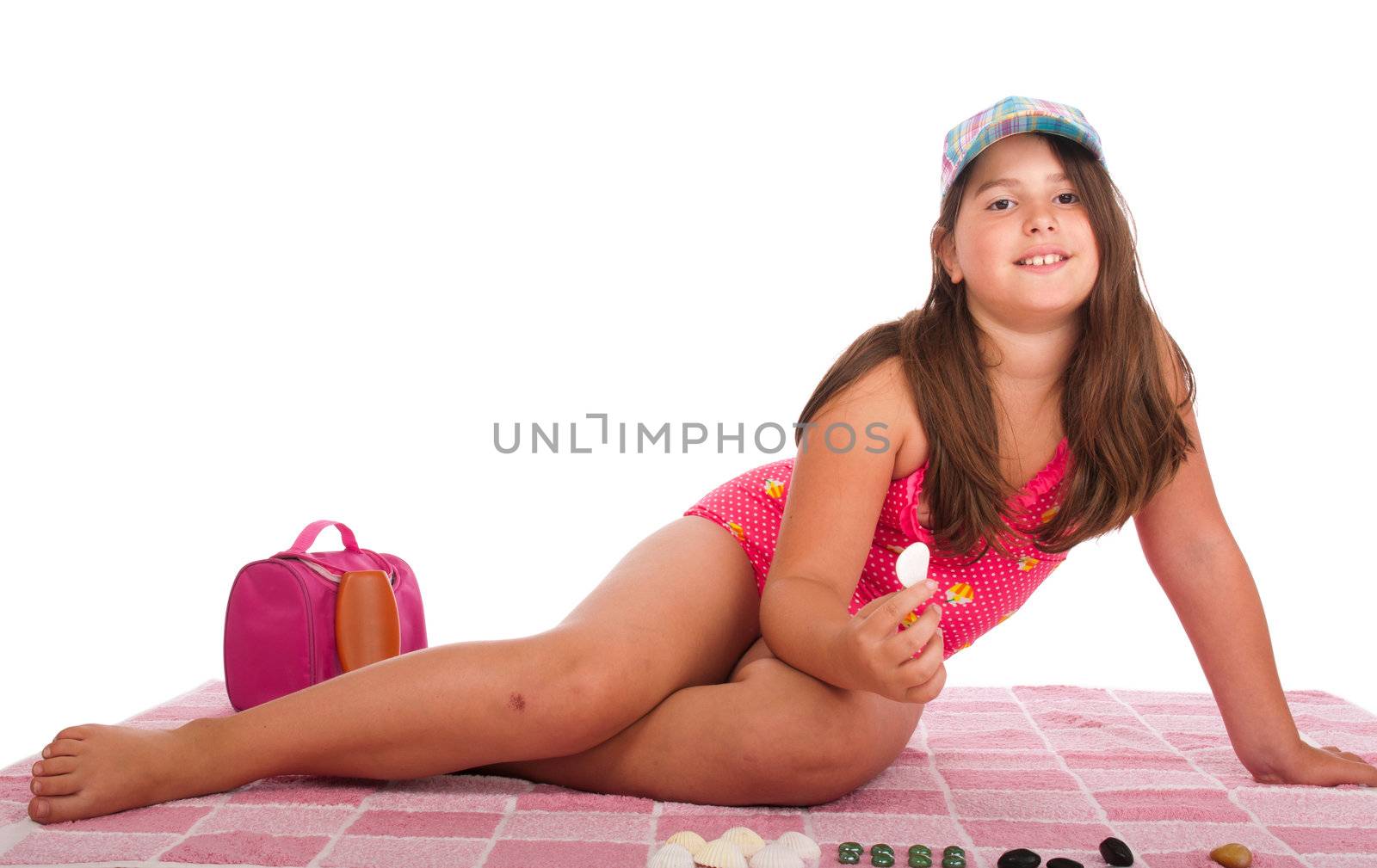 beautiful brunette teenage girl in swimsuit at the beach playing with little stones (studio setting with towel, bag and sun lotion, isolated on white background)