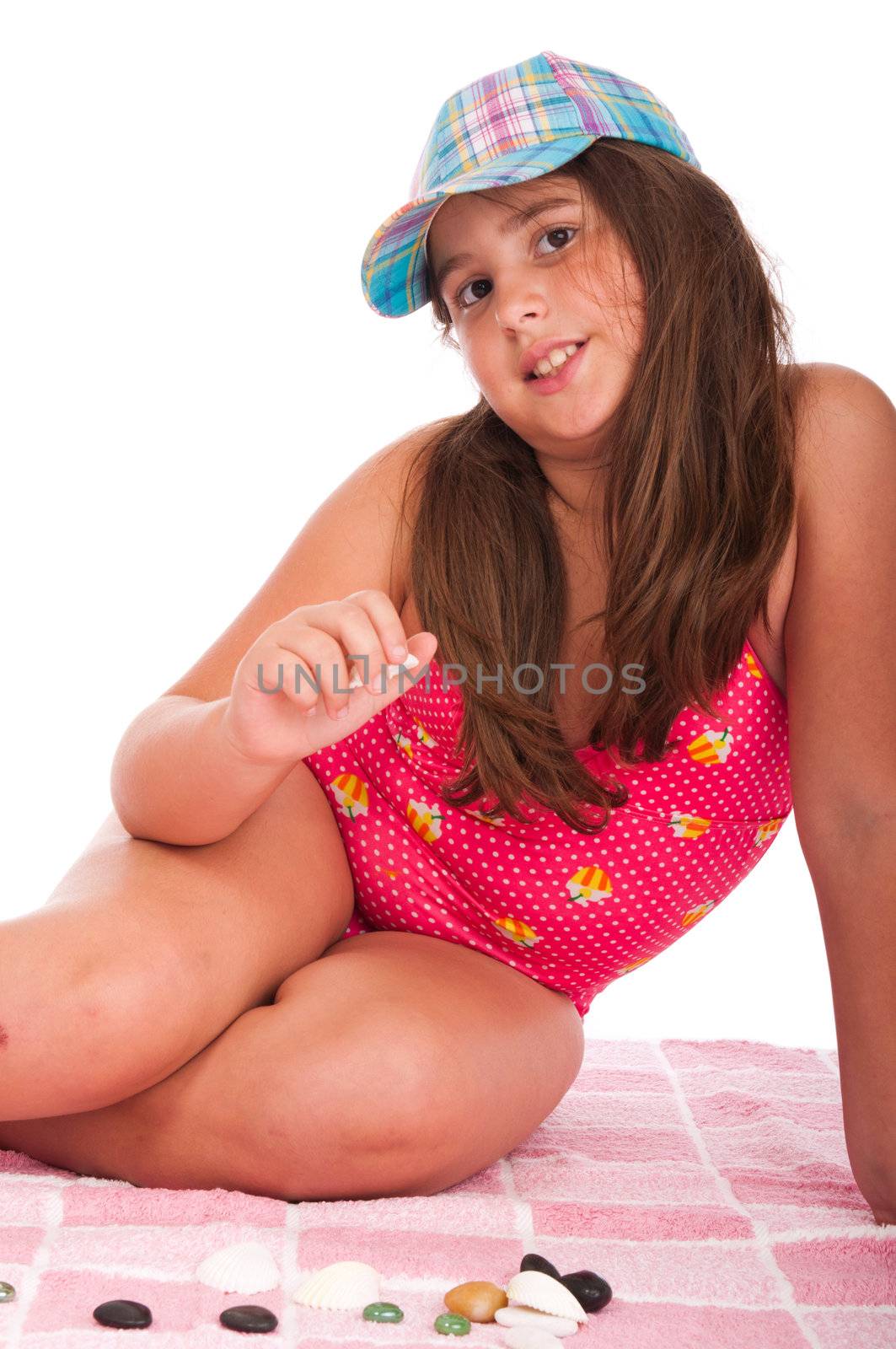 beautiful brunette teenage girl in swimsuit at the beach playing with little stones (studio setting with towel and pebbles, isolated on white background)
