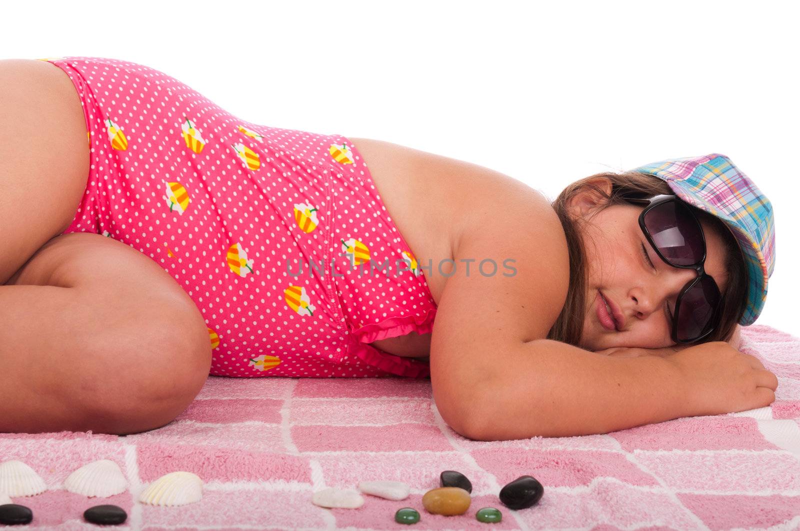 beautiful brunette teenage girl in swimsuit sleeping at the beach (studio setting with towel and pebbles, isolated on white background)
