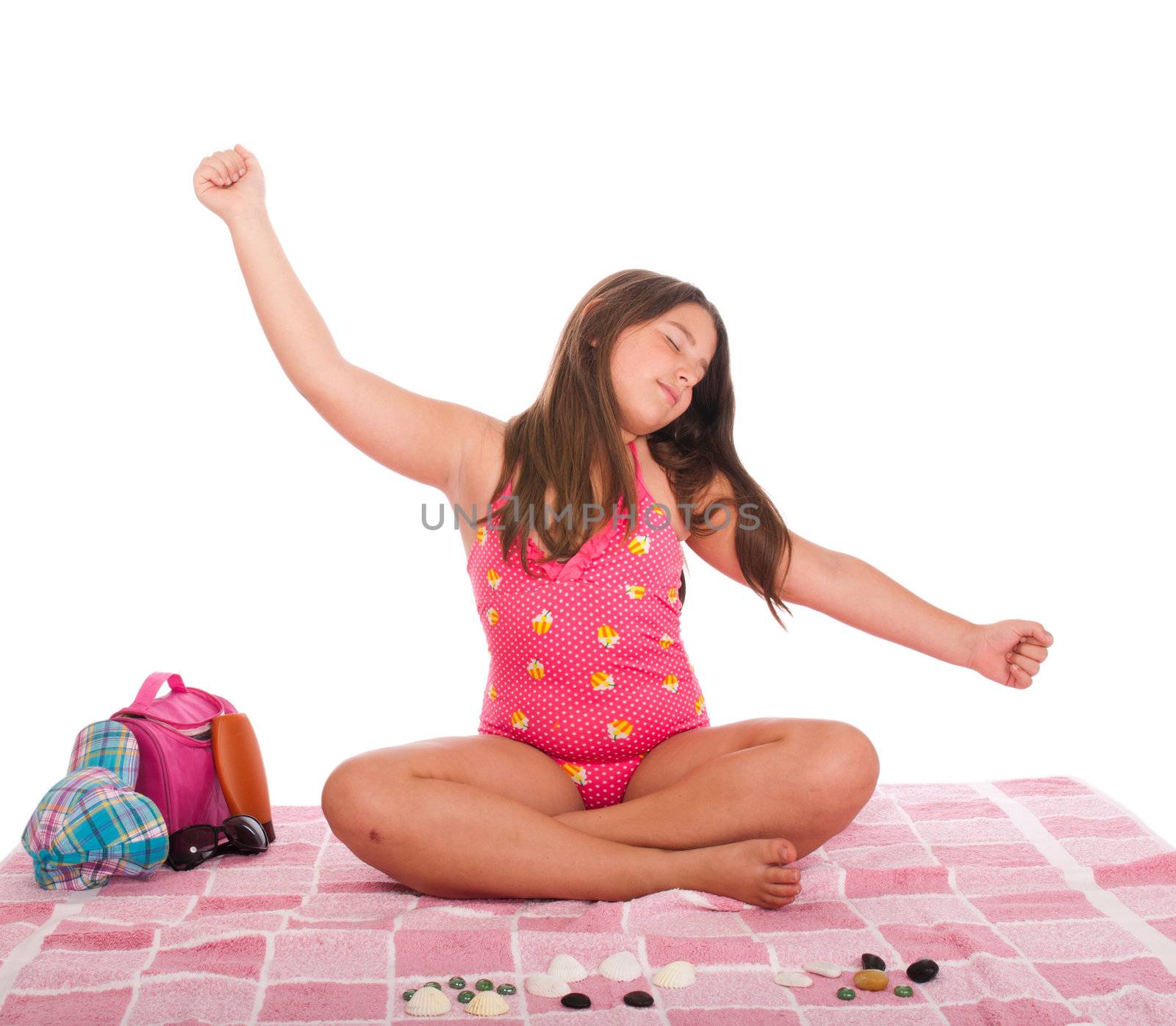 beautiful brunette teenage girl in swimsuit at the beach relaxing with arms raised (studio setting with cap, towel, bag, sun lotion, sunglasses and stones) isolated on white background