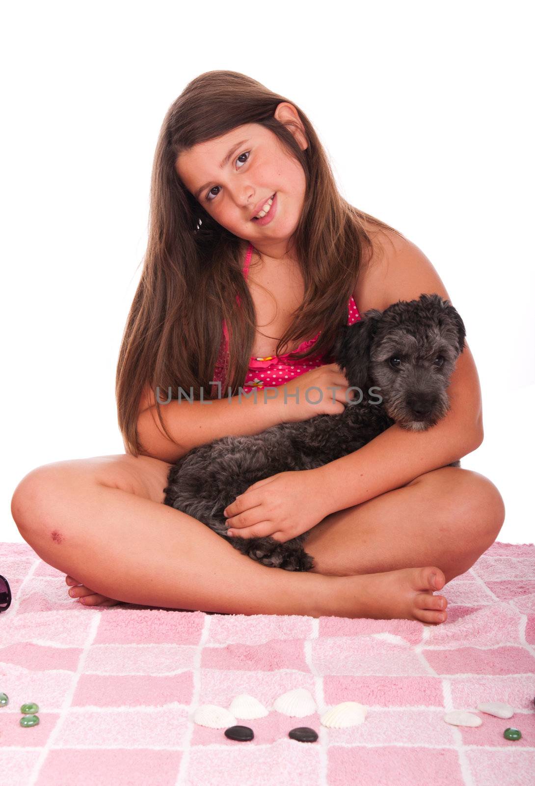 smiling brunette teenage girl in swimsuit at the beach with her shipoo dog (studio setting with pink towel and little stones) isolated on white background