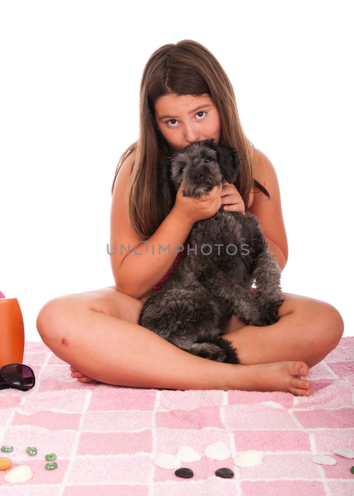 smiling brunette teenage girl in swimsuit at the beach kissing her shipoo dog (studio setting with beach items and little stones) isolated on white background