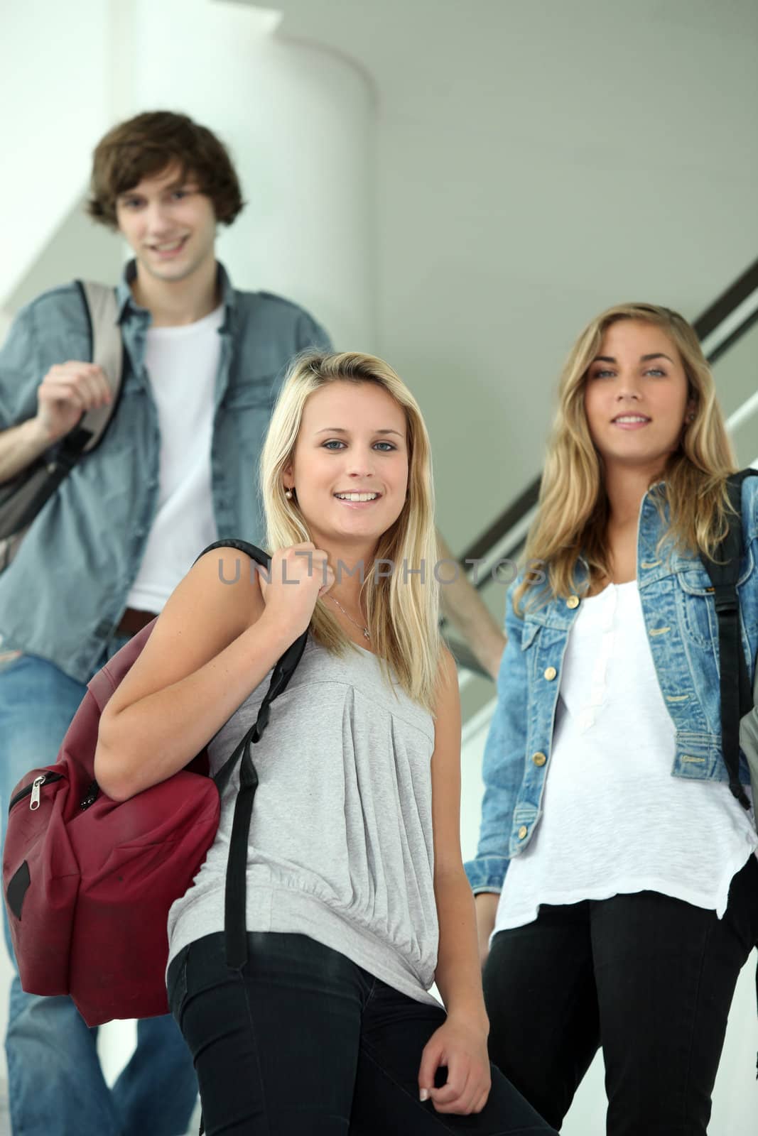 Three smiling students walking down interior stairs by phovoir
